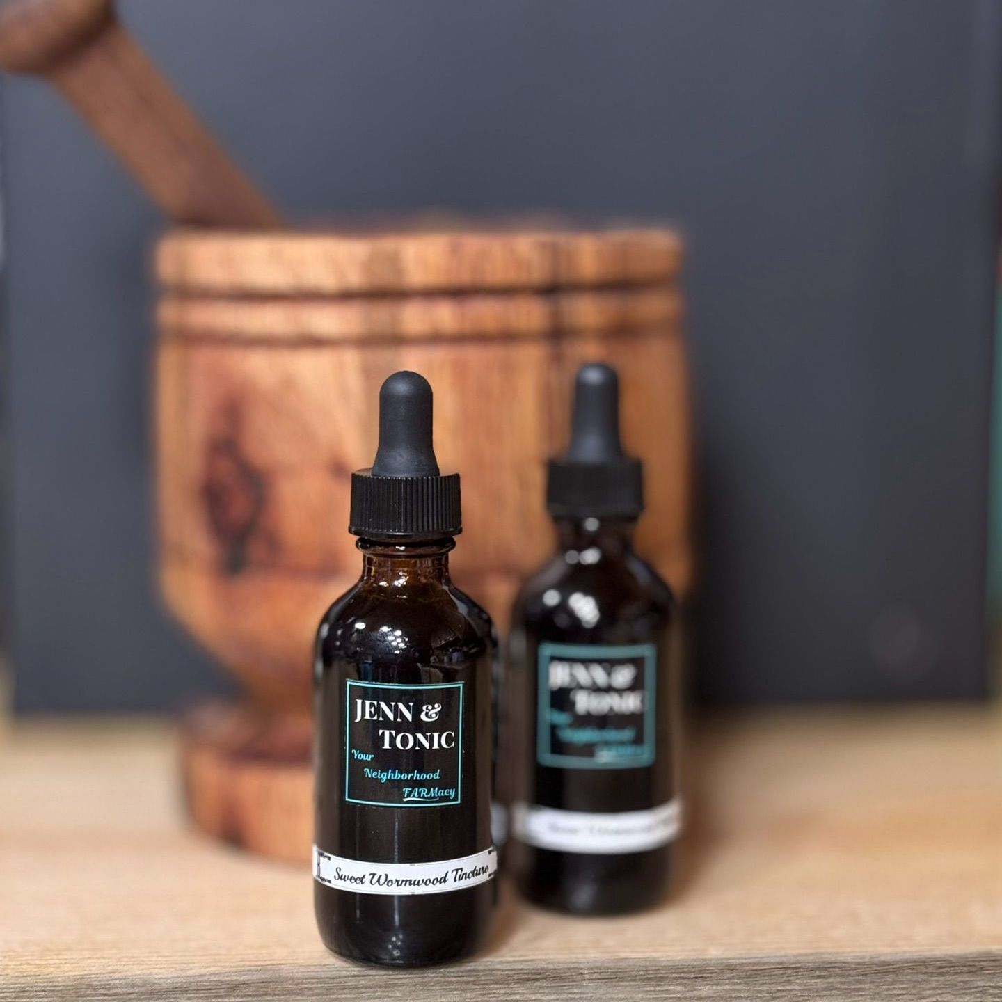 Two bottles of liquid are sitting on a wooden table next to a mortar and pestle.