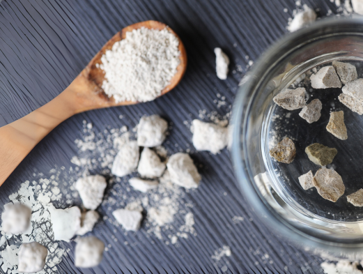 A wooden spoon filled with zeolite powder next to a glass of water
