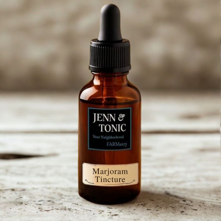 An amber glass dropper bottle labeled "Jenn & Tonic" and "Marjoram Tincture" sitting on a light wooden surface.