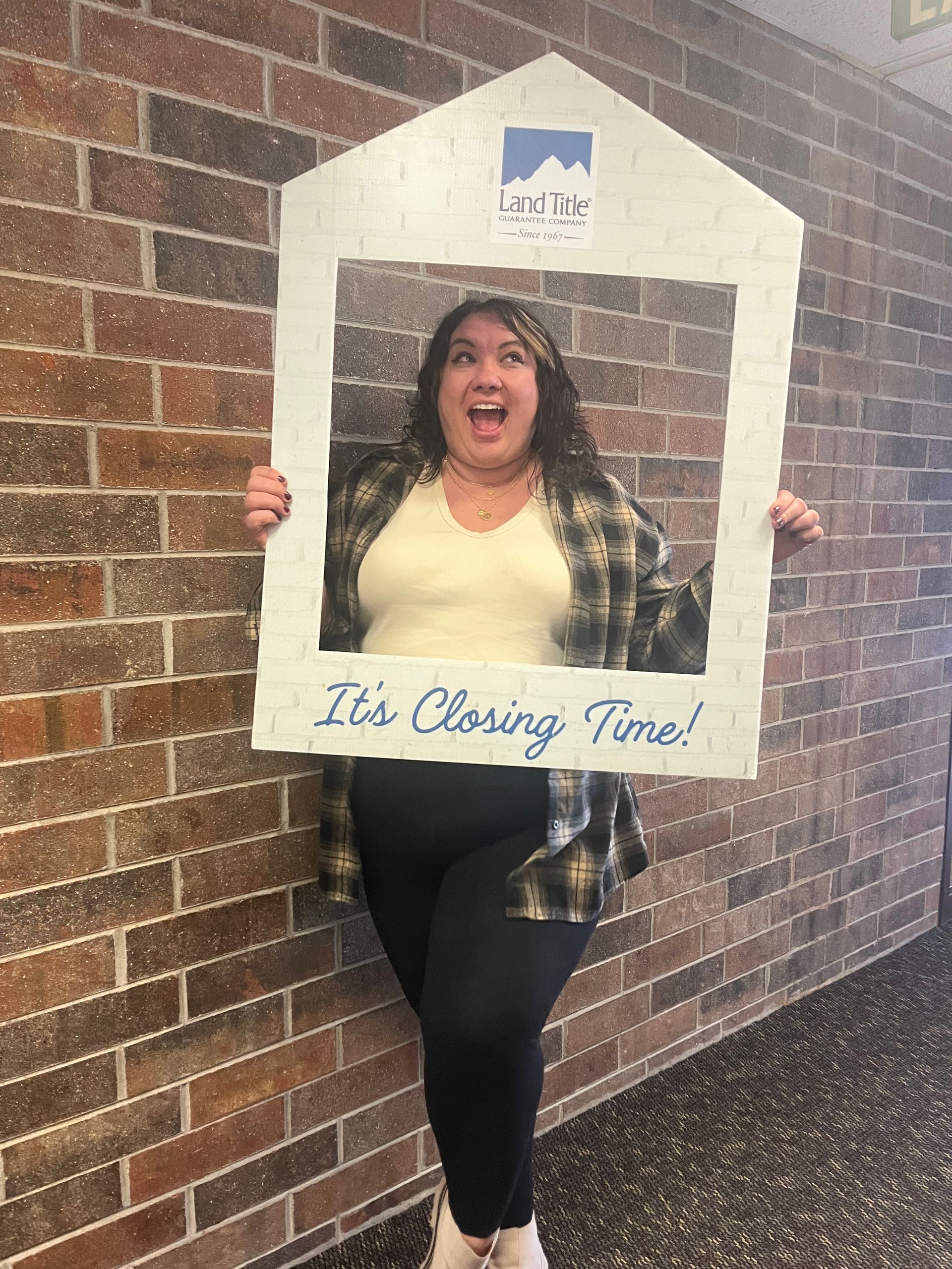 An excited woman posing with a large sign in front of a brick wall