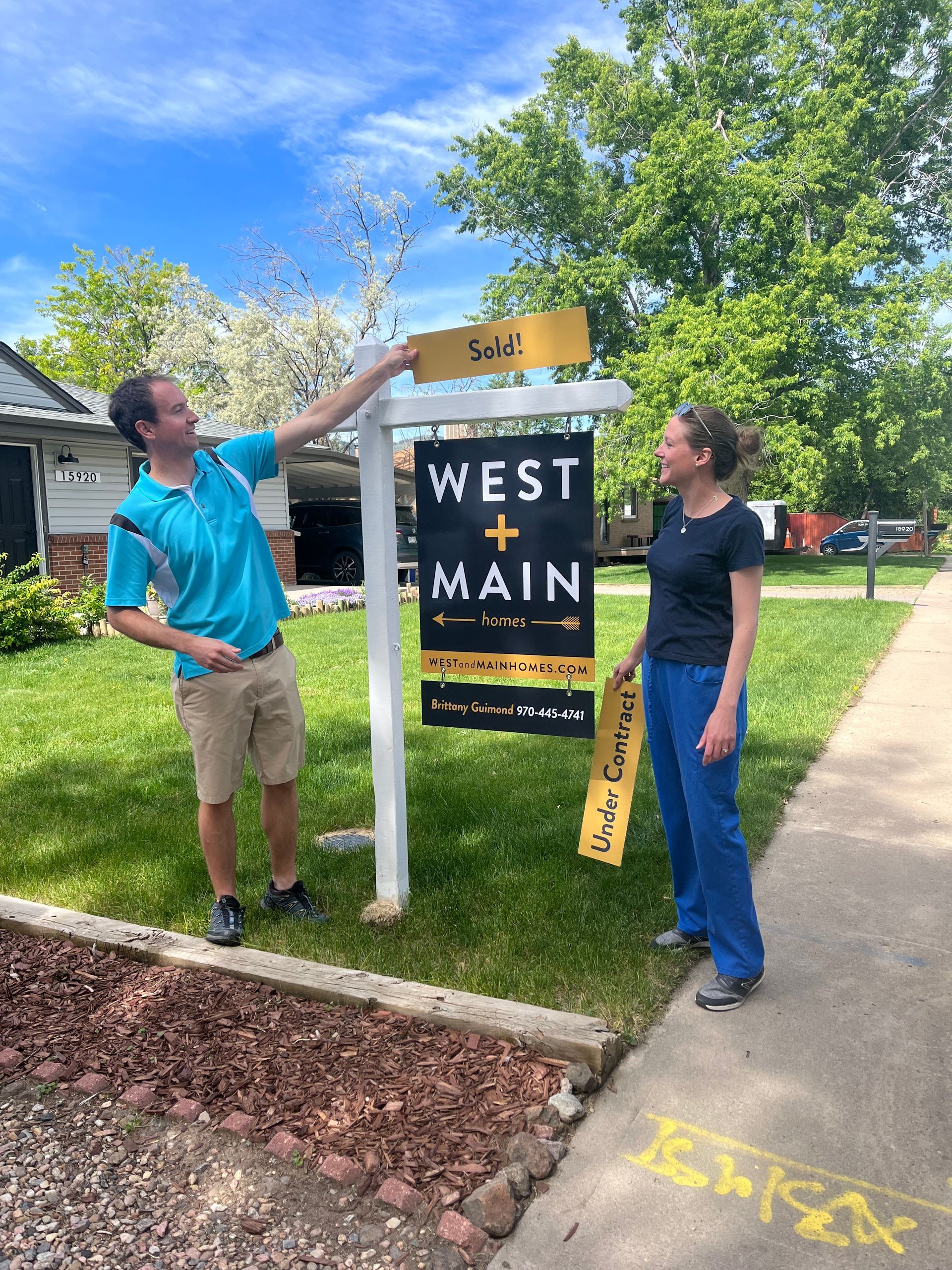 two people hanging a sold sign in the front yard