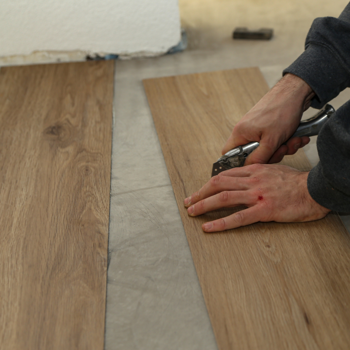 Person measuring and cutting a wood plank on a floor beside an unfinished strip of concrete