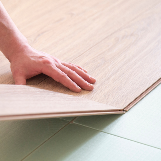 Hand placing a light wood panel onto a tiled floor edge