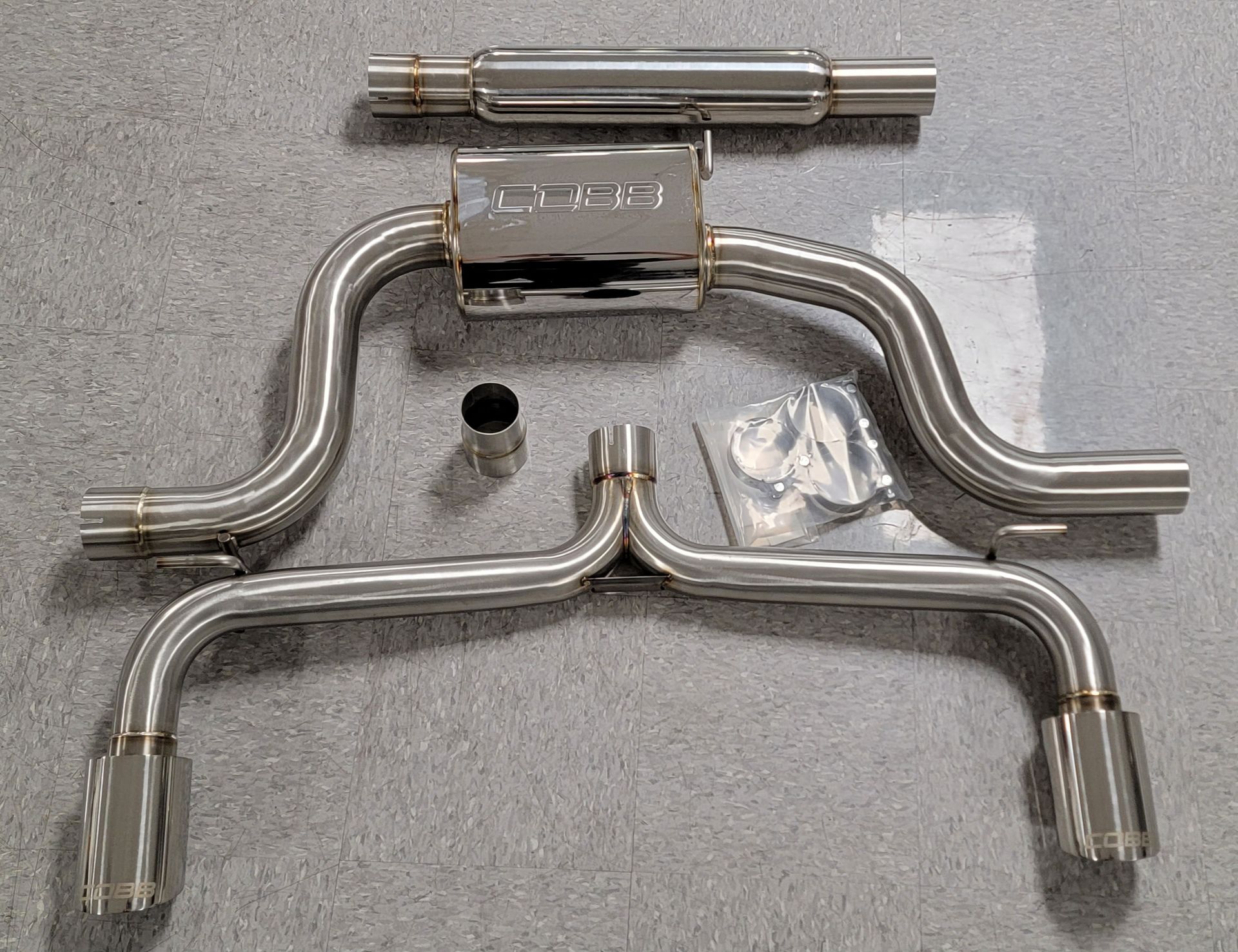 A stainless steel exhaust pipe is sitting on a carpeted floor | Griffin Motorwerke