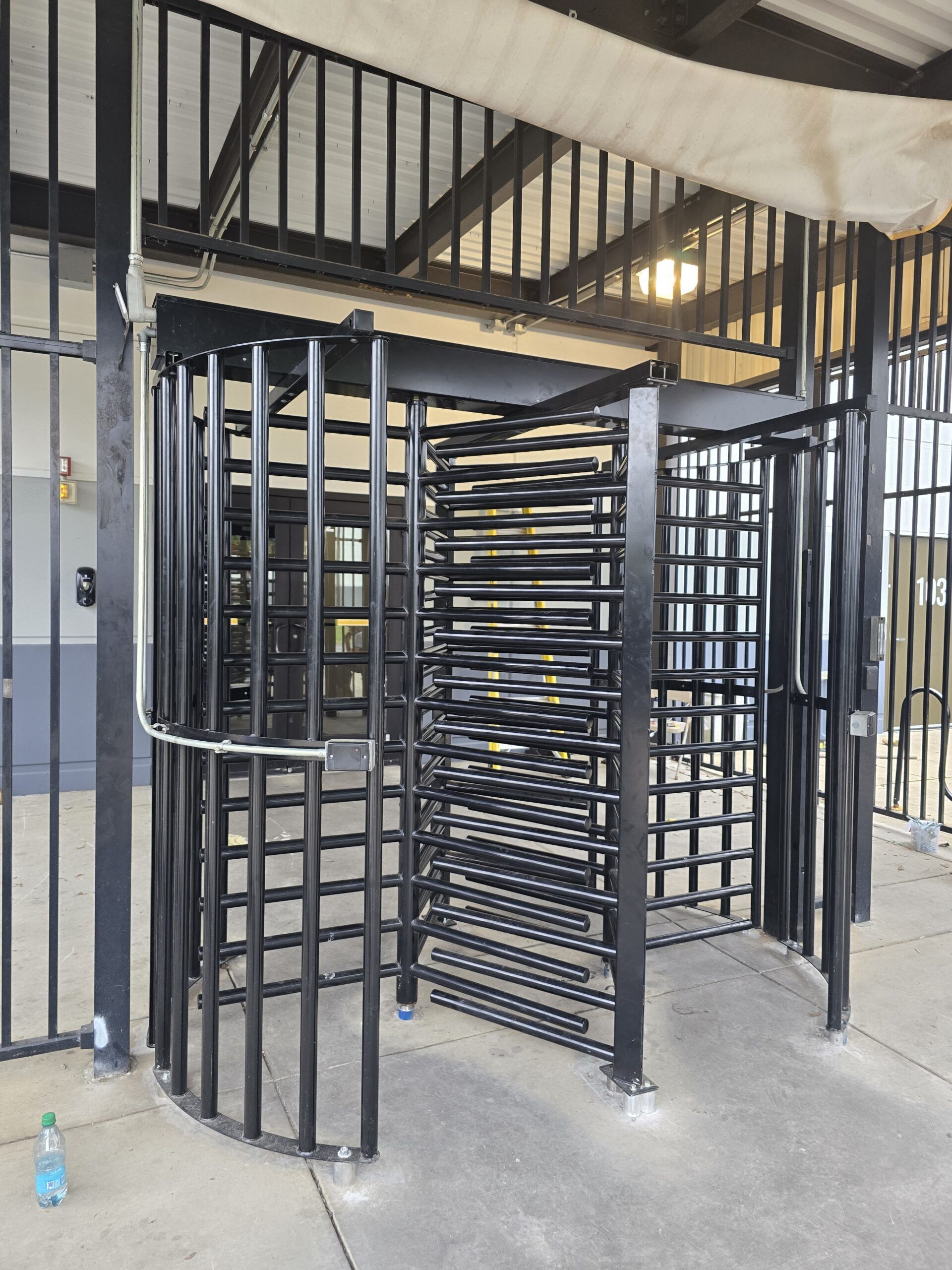 Black turnstile with multiple vertical bars, likely for access control, under a metal awning.