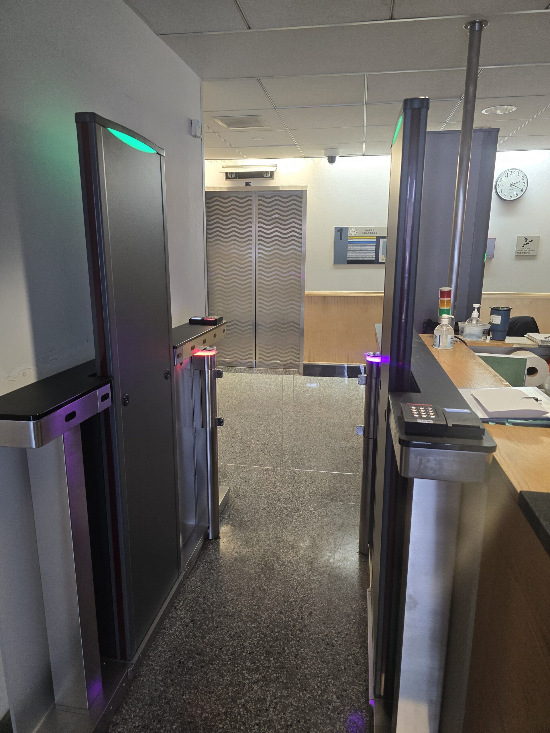 Security turnstiles and elevator in a bank lobby. A green light signals access.