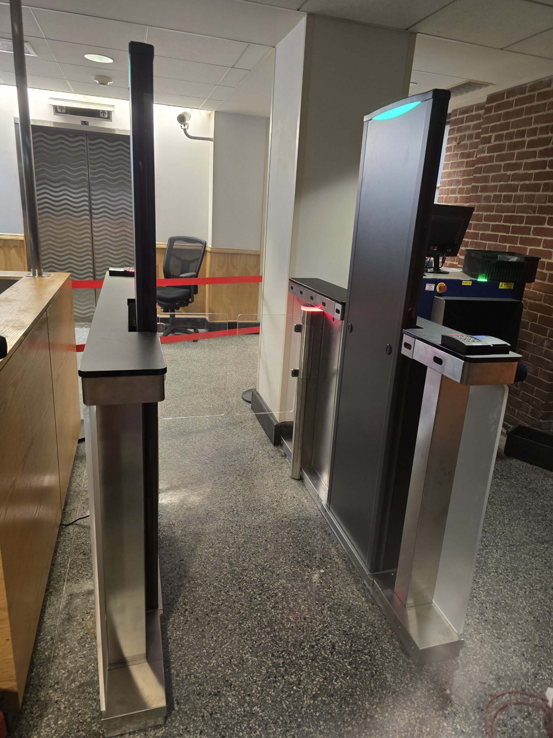 A security turnstile in a building entrance. A metal gate with a screen and a long arm.