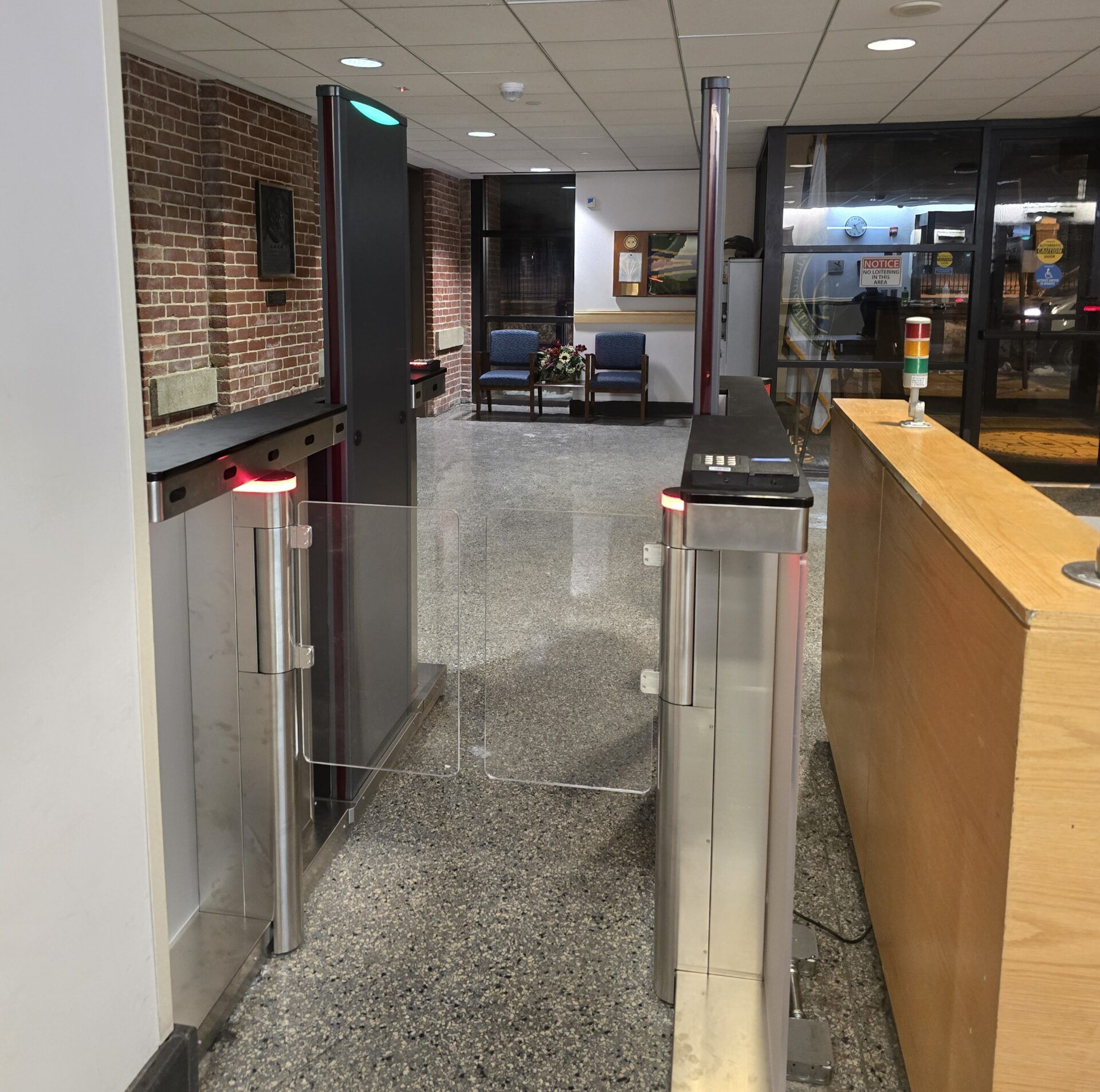 Security entrance with two turnstiles in a building. Granite floor. Brick wall in background.