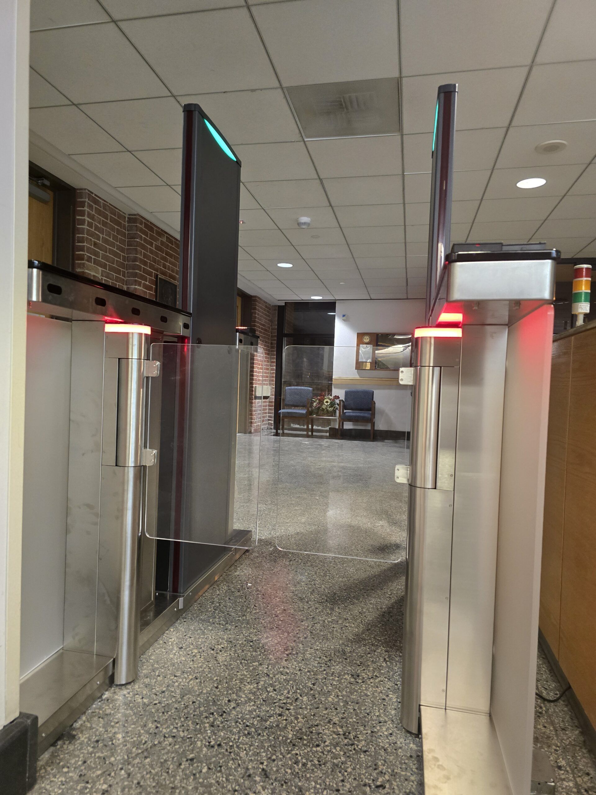 Two silver security turnstiles with red lights in a hallway.