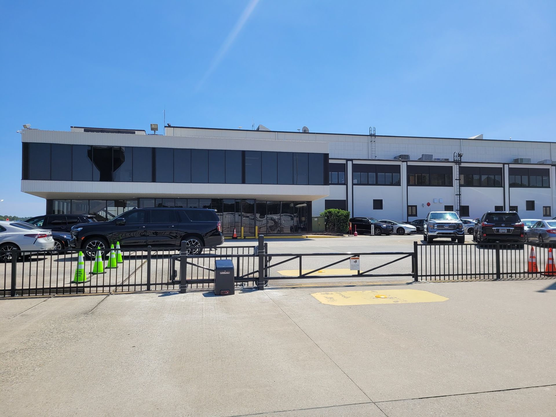 Exterior of a building with a black SUV parked in front of it. Cars and a security gate are also visible.