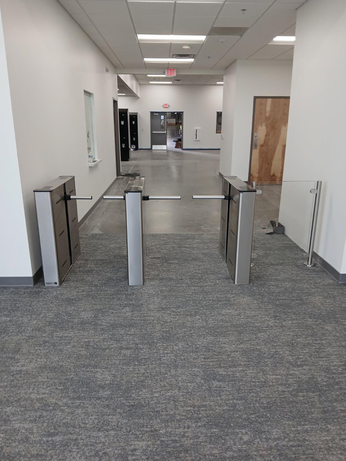 Hallway with silver turnstiles, gray carpet, and white walls.