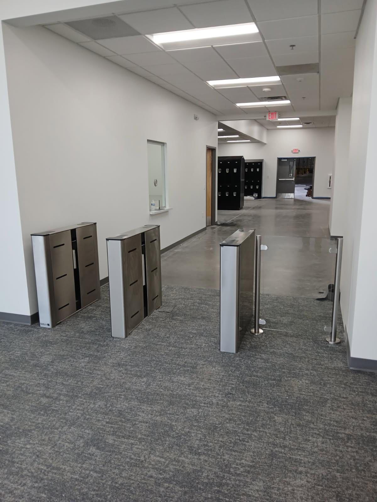 Hallway with security turnstiles, gray carpet, white walls, and lockers.