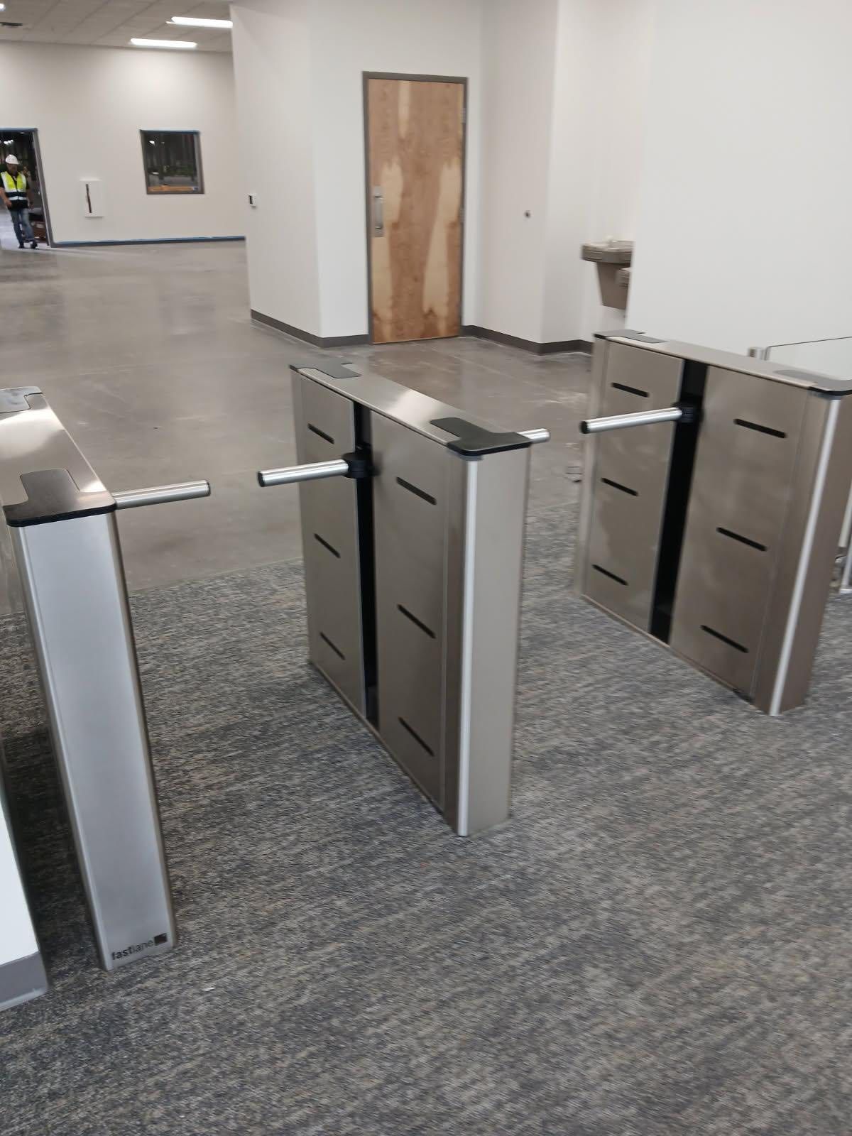 Three silver security turnstiles on gray carpet. A wooden door is in the background.