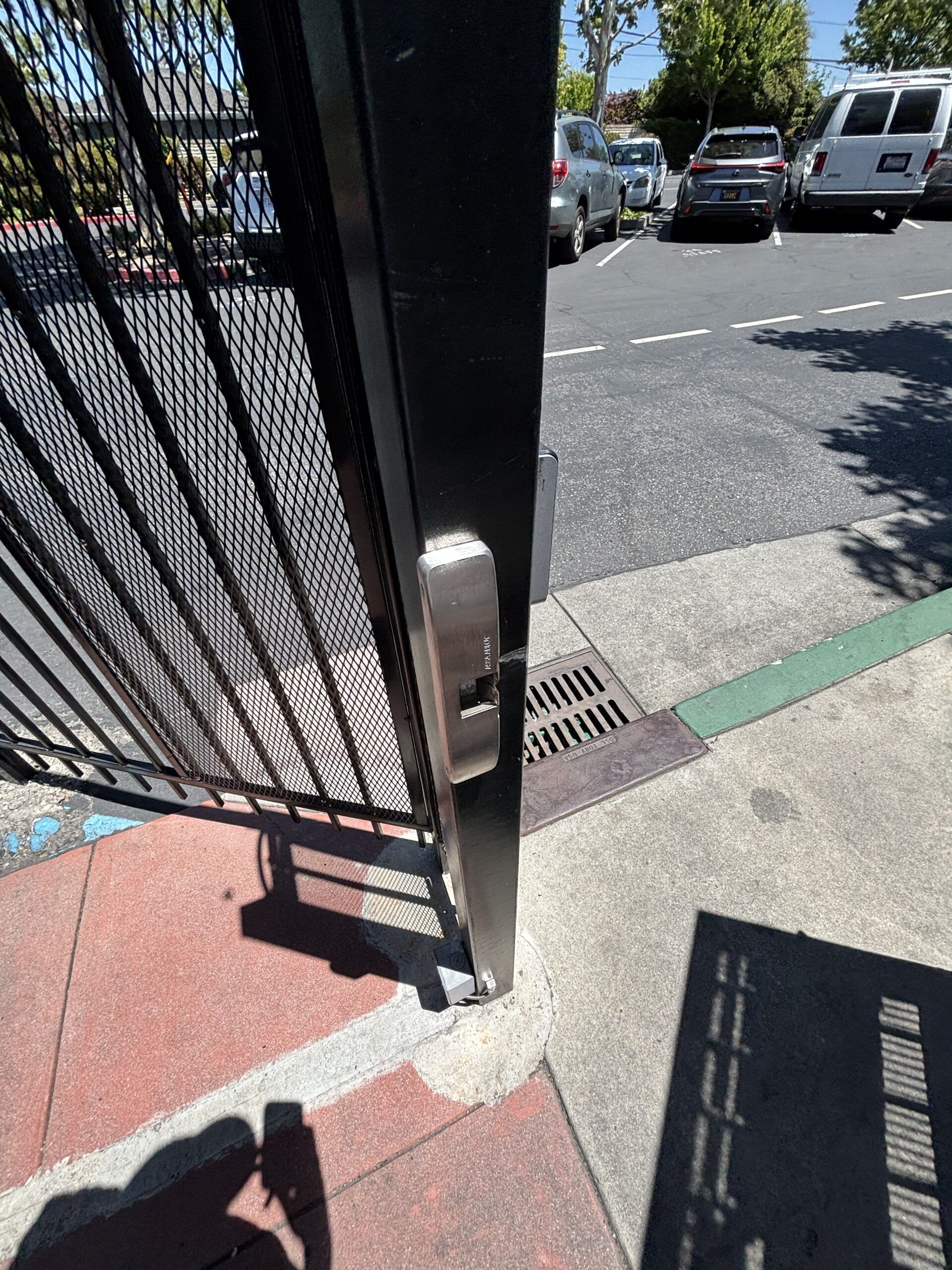 Black metal gate with lock, concrete, and parking lot in the background.