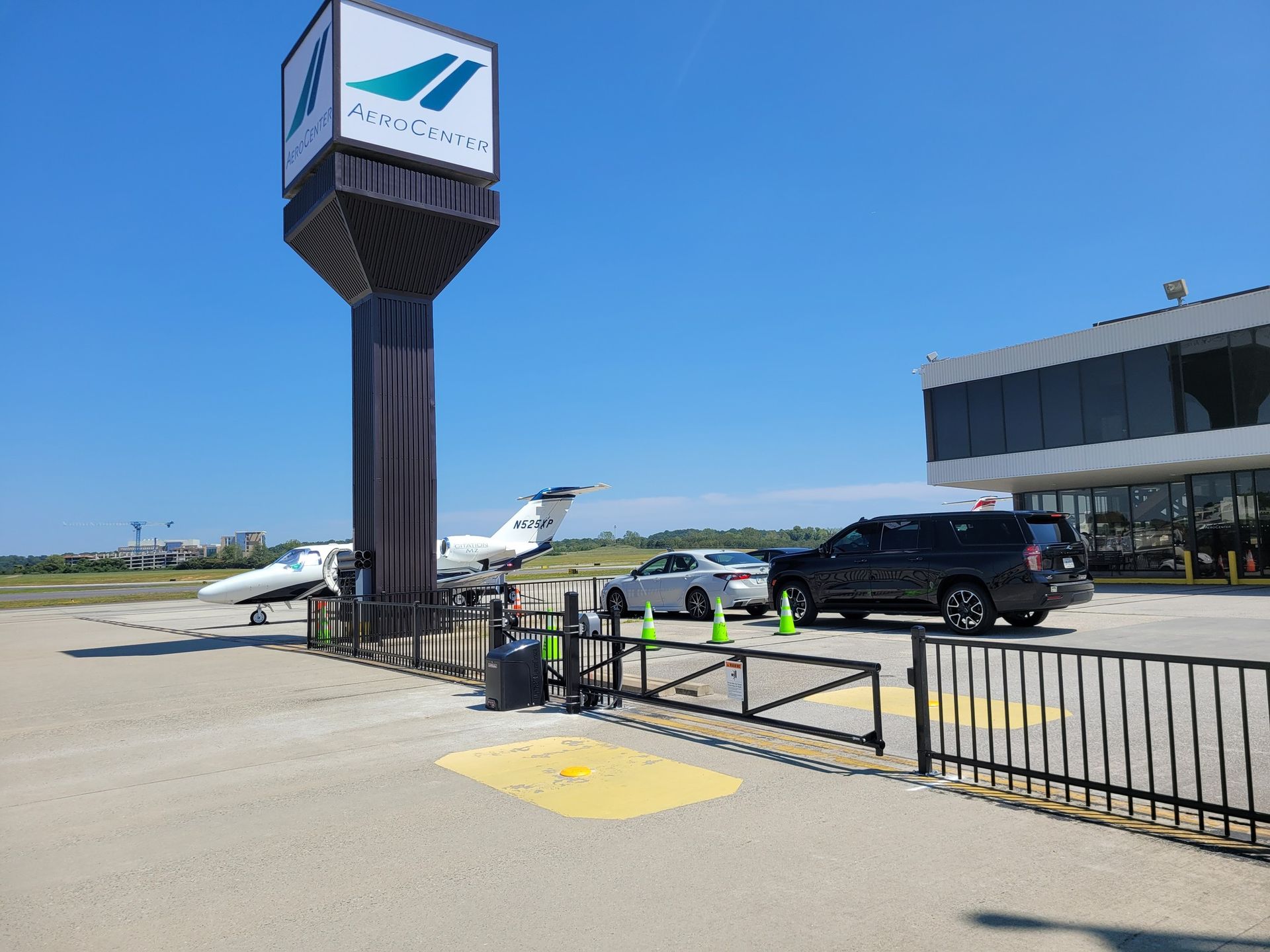 Airport entrance with sign, planes, cars, and building against a blue sky.