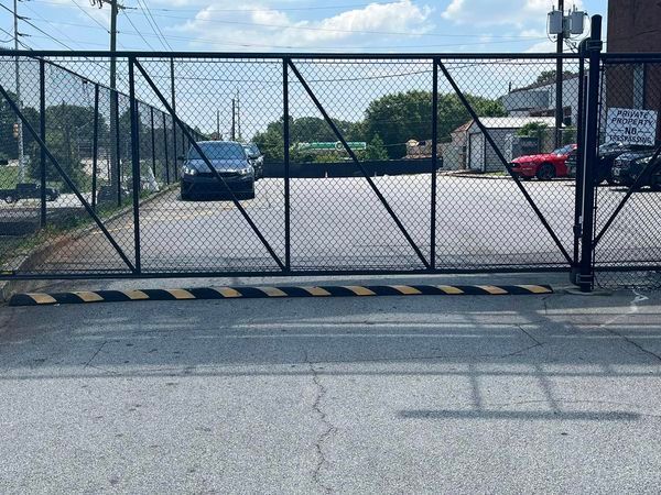 Black gate with chain link fence, a car parked inside, speed bump, overcast sky.