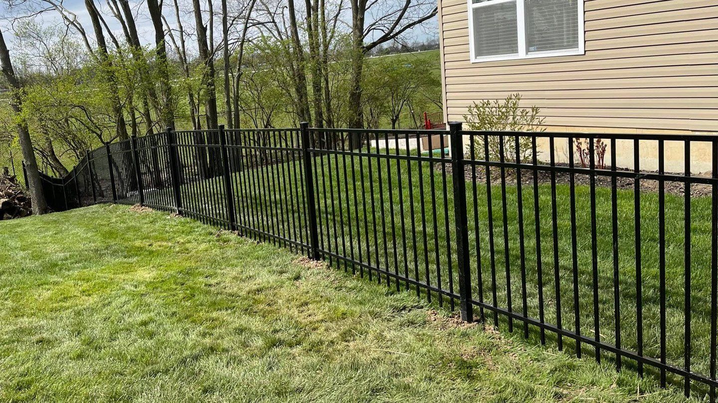A black  steel fence surrounds a lush green lawn in front of a house.