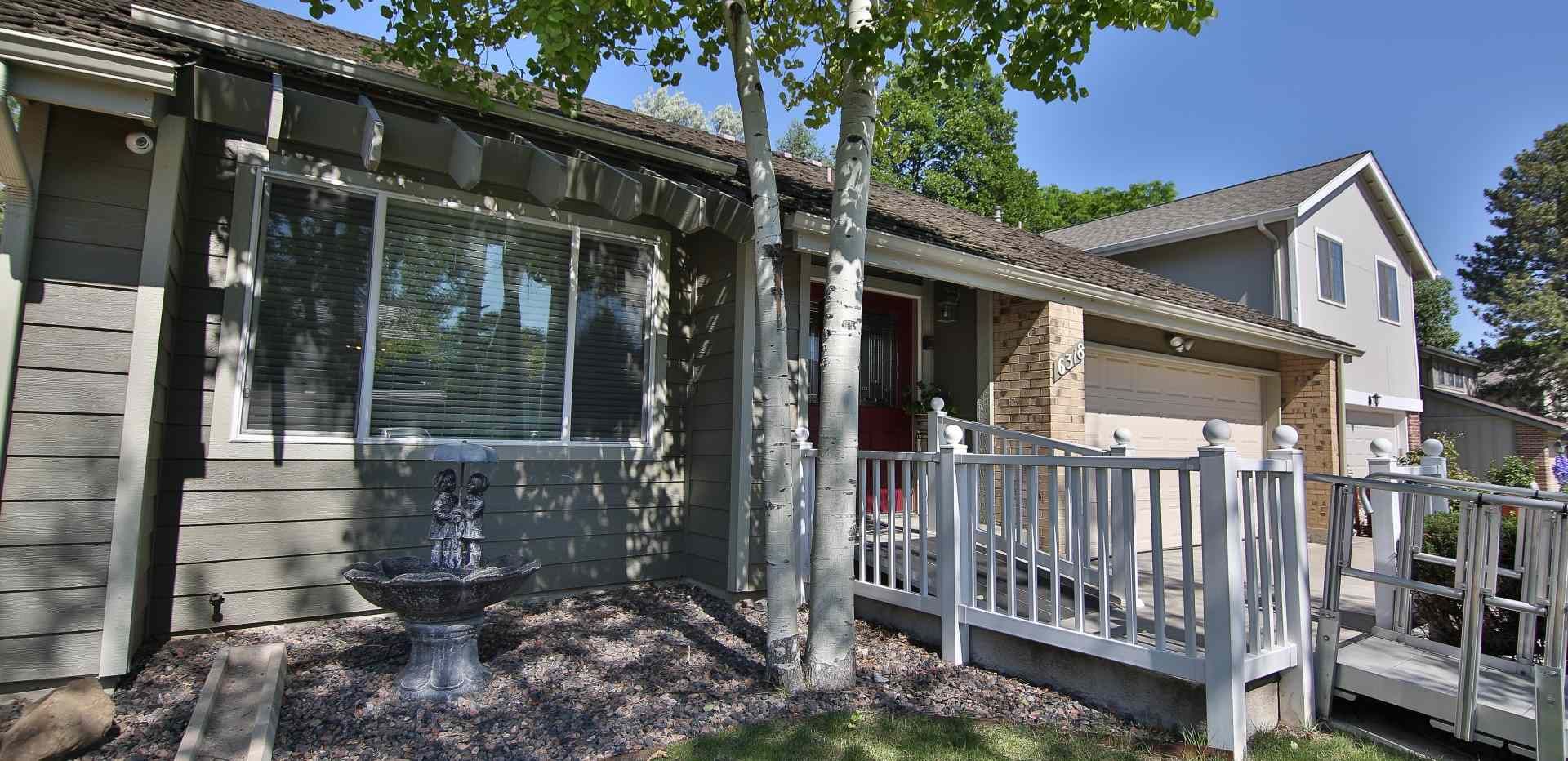 House exterior with stone facade, white porch, and two-story gray structure in the background.