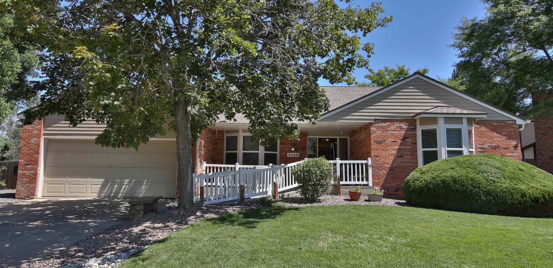 Brick house with a garage, porch, and green lawn, partly shaded by a large tree.