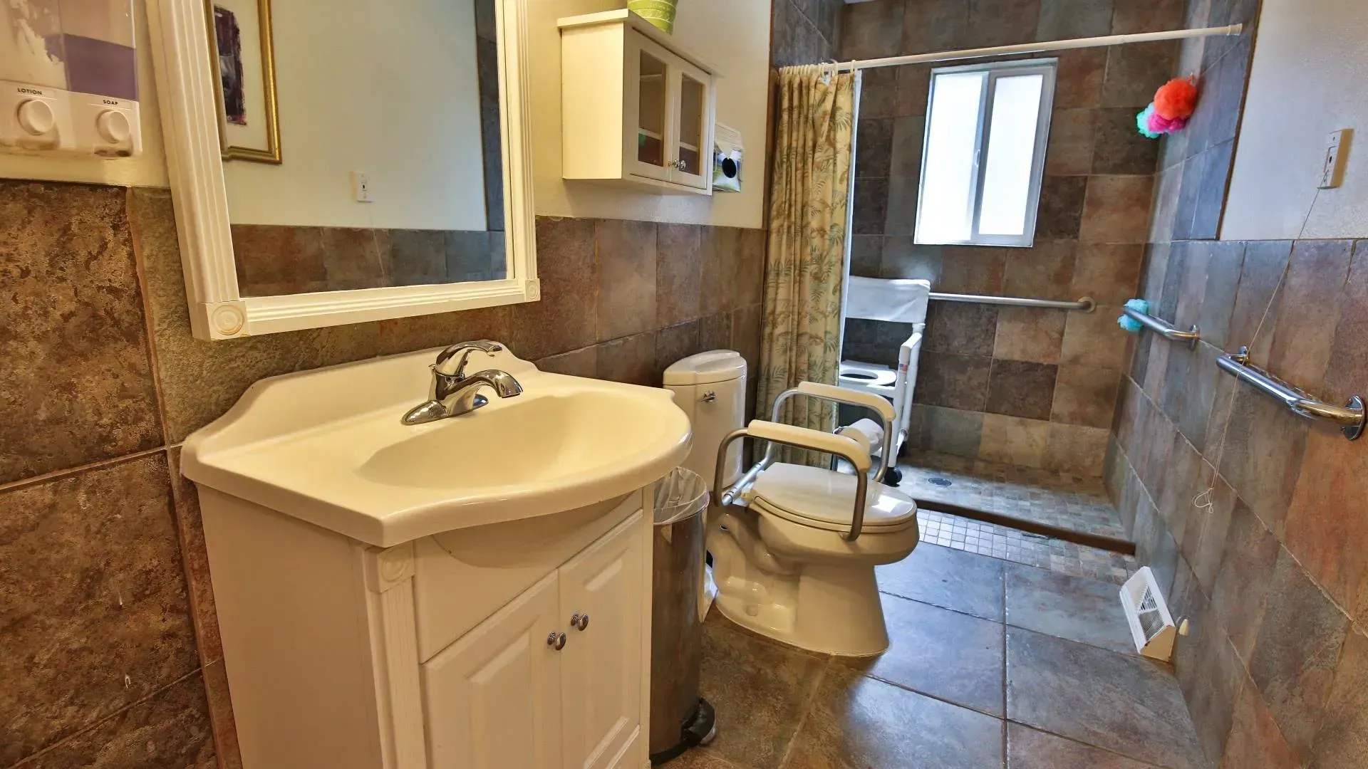 Bathroom with a white vanity, toilet with grab bars, and tiled walls.