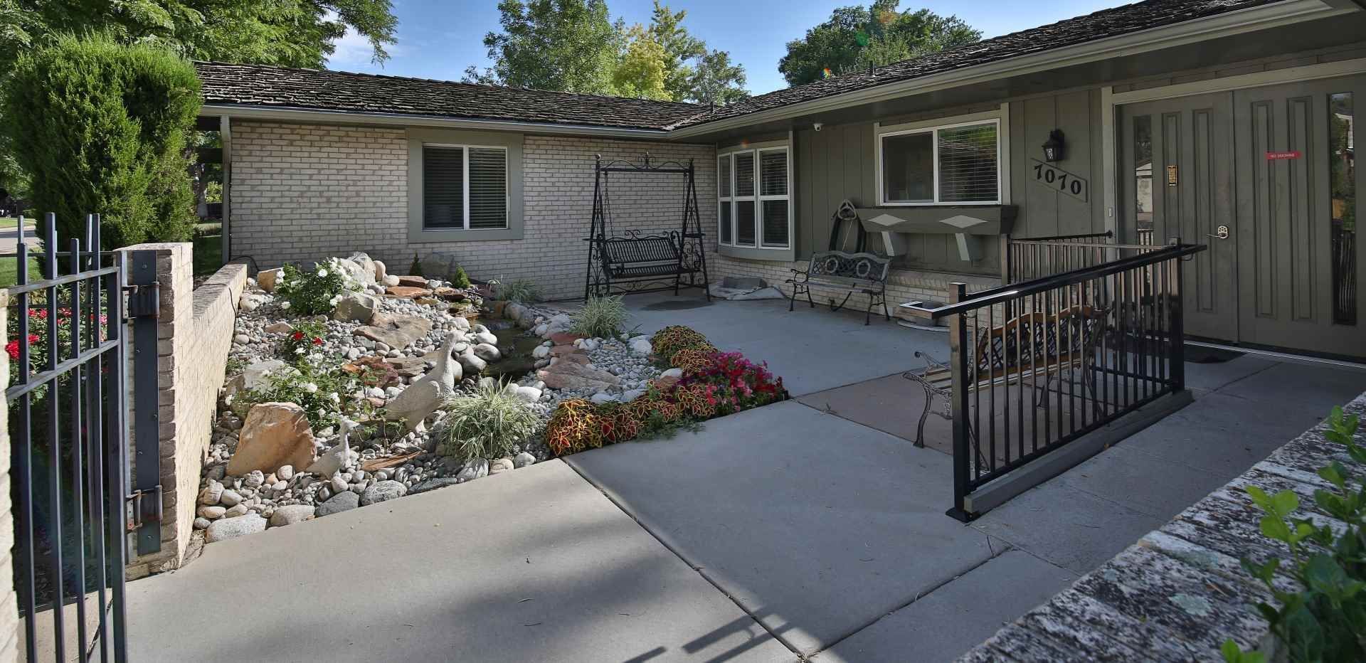 A house with a concrete walkway, flower beds, and benches. There's a handicap ramp.