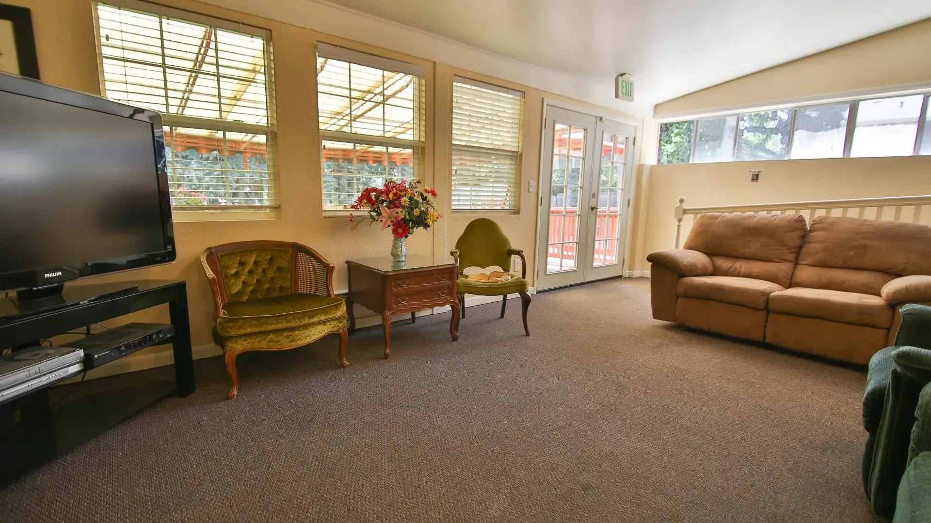 Living room with two green armchairs, brown sofa, TV, windows, and double doors.