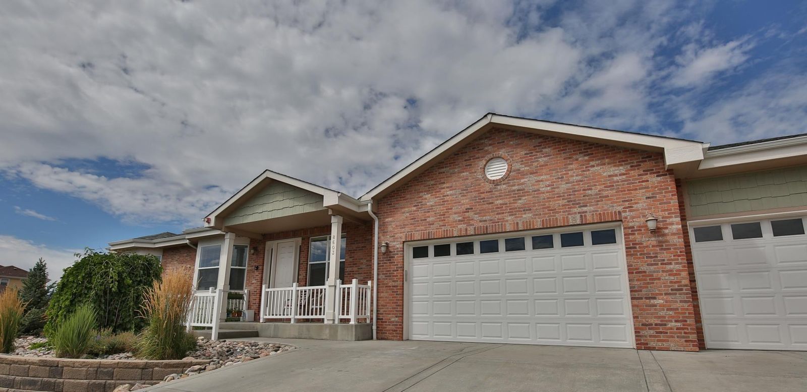 A brick house with a white garage door and a front porch under a partly cloudy sky.
