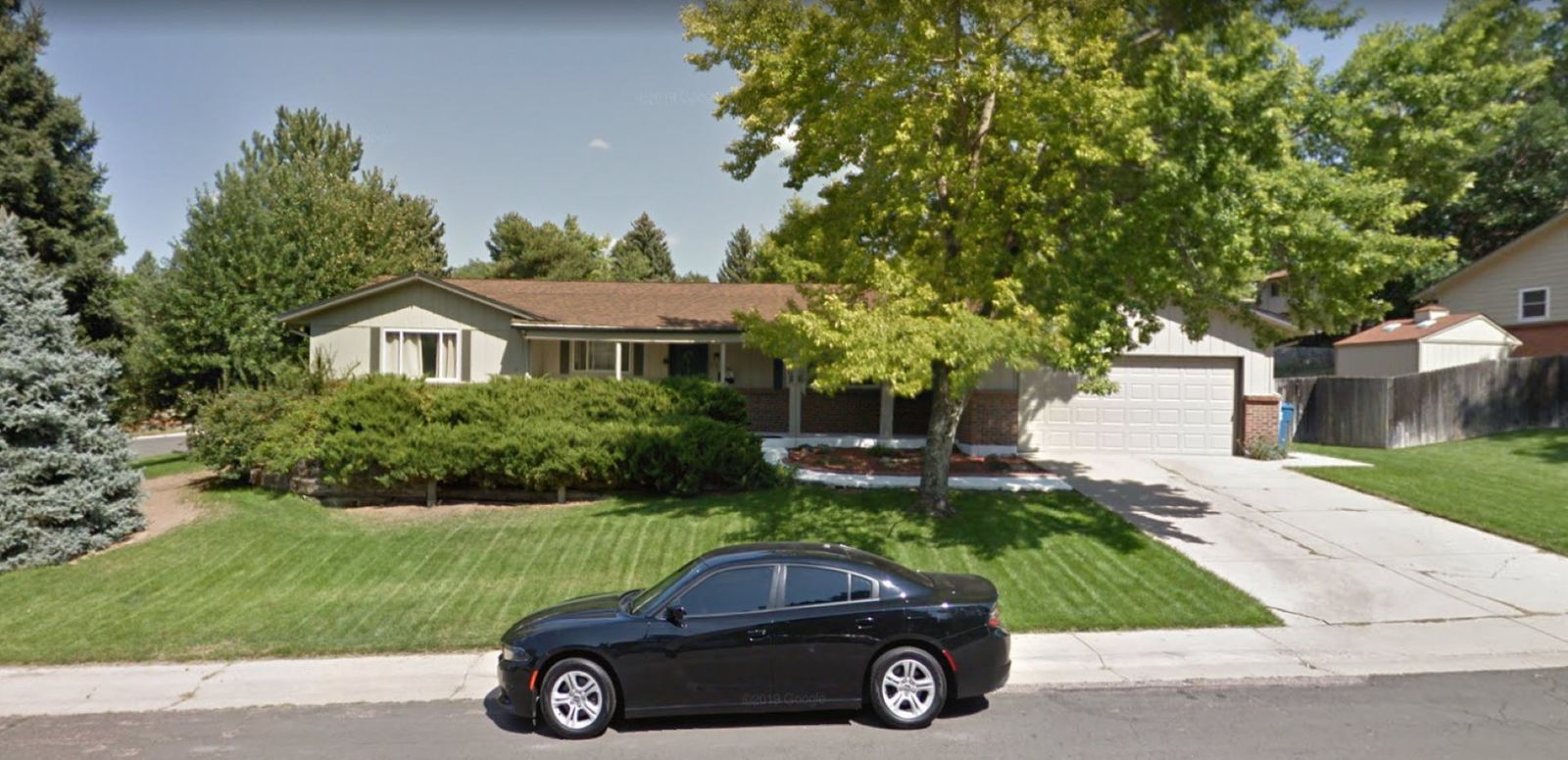 Black car parked in front of a light-colored house with a brown roof and green lawn. Blue sky.