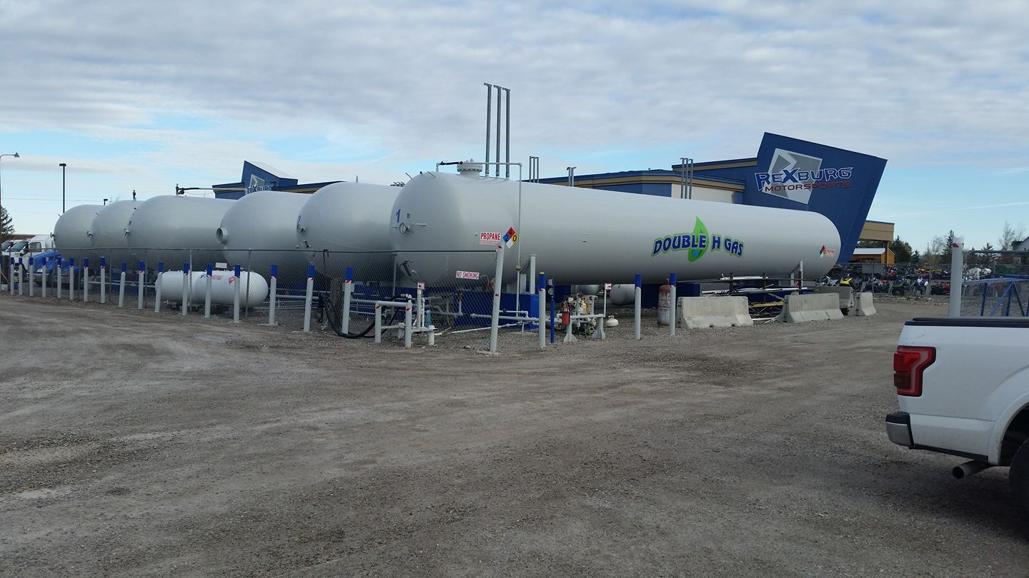 A white truck is parked in front of a row of propane tanks.