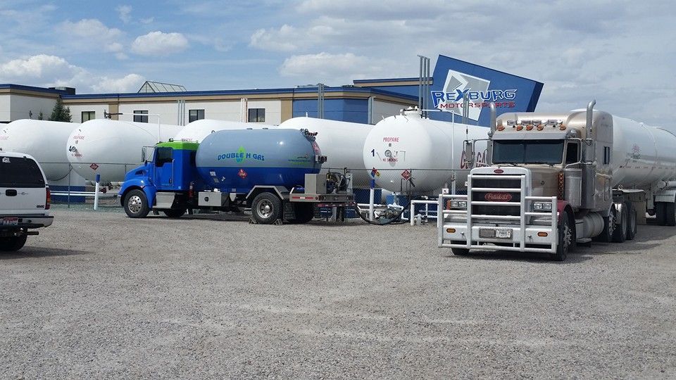 A row of trucks are parked in a gravel lot in front of a building.
