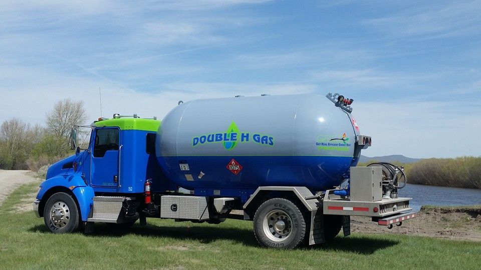 A blue and gray propane truck is parked in a grassy field.