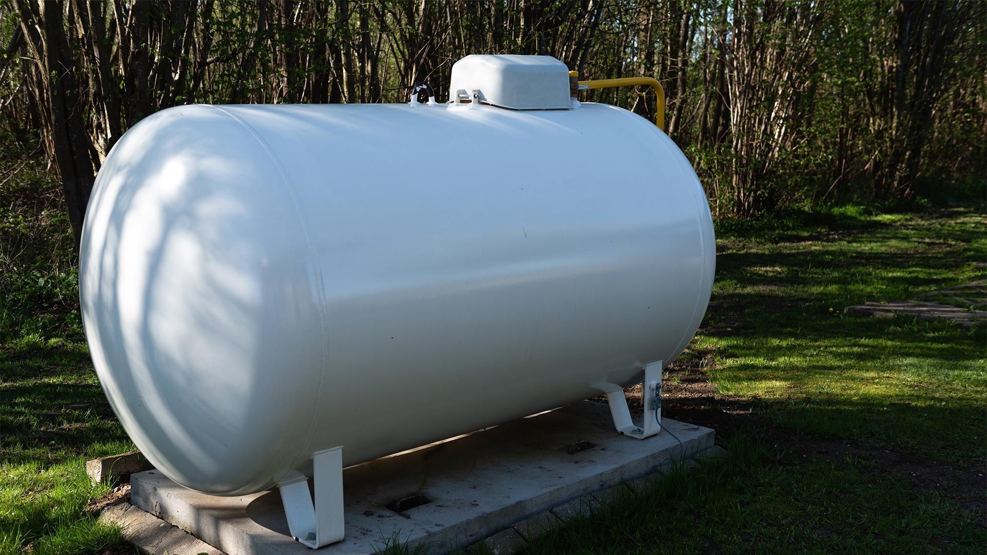 A large white propane tank is sitting on top of a concrete platform in the grass.