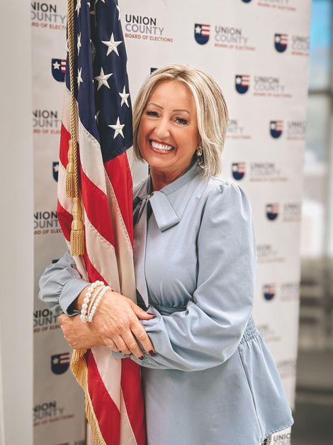 Woman in blue holding American flag, smiling in front of a backdrop with logos.
