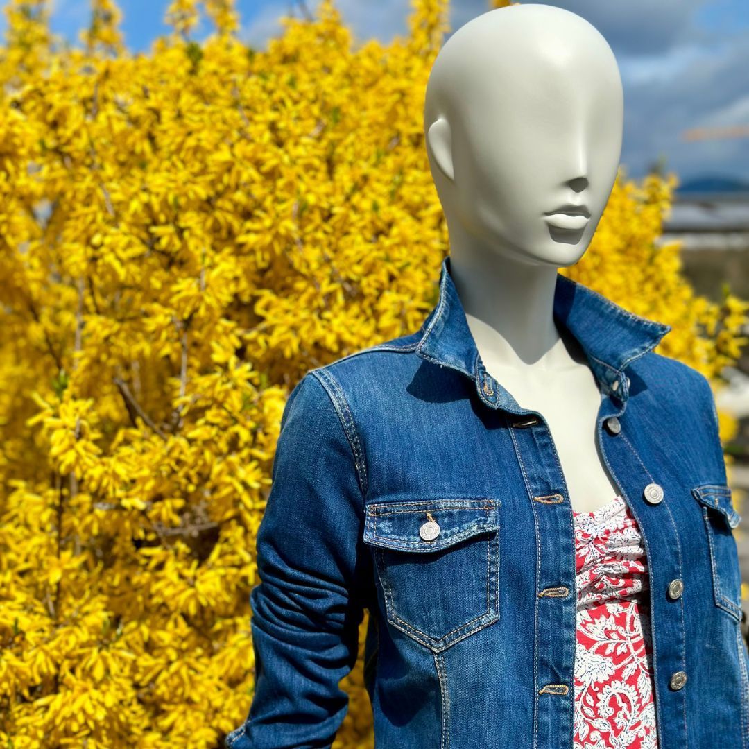 Eine Schaufensterpuppe in einer Jeansjacke steht vor gelben Blumen