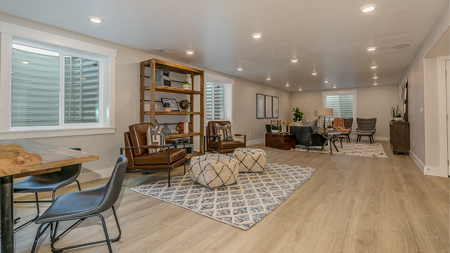 a basement family room with hardwood floors , chairs , a table and a rug .