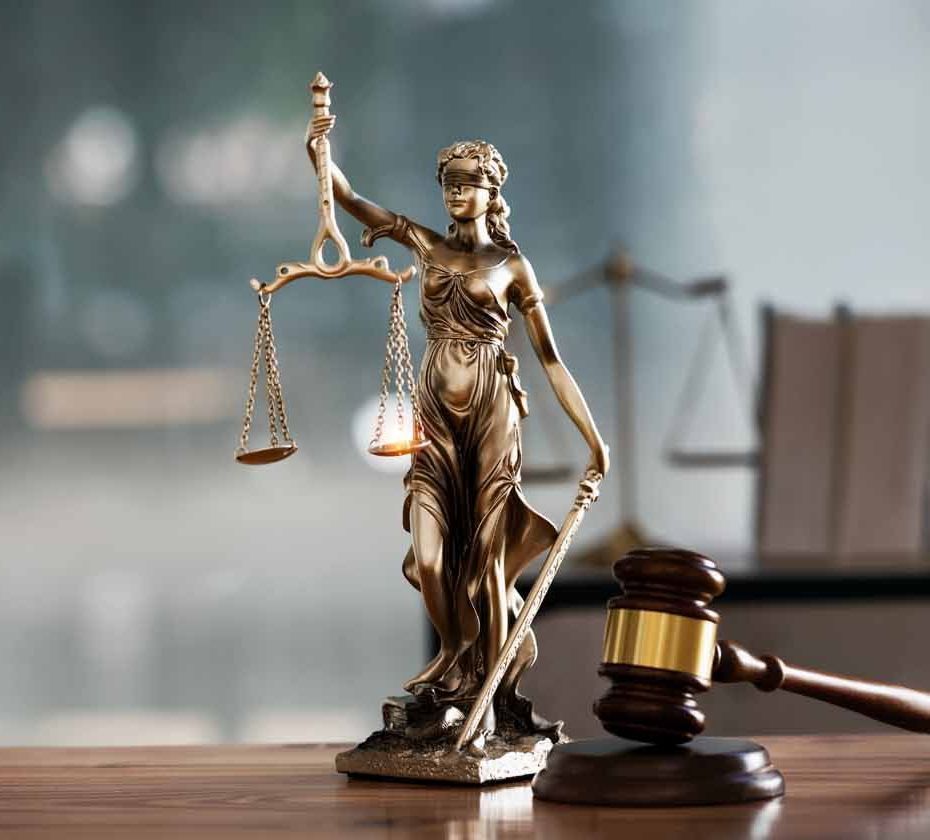 A statue of justice is sitting on a wooden table next to a judge 's gavel.