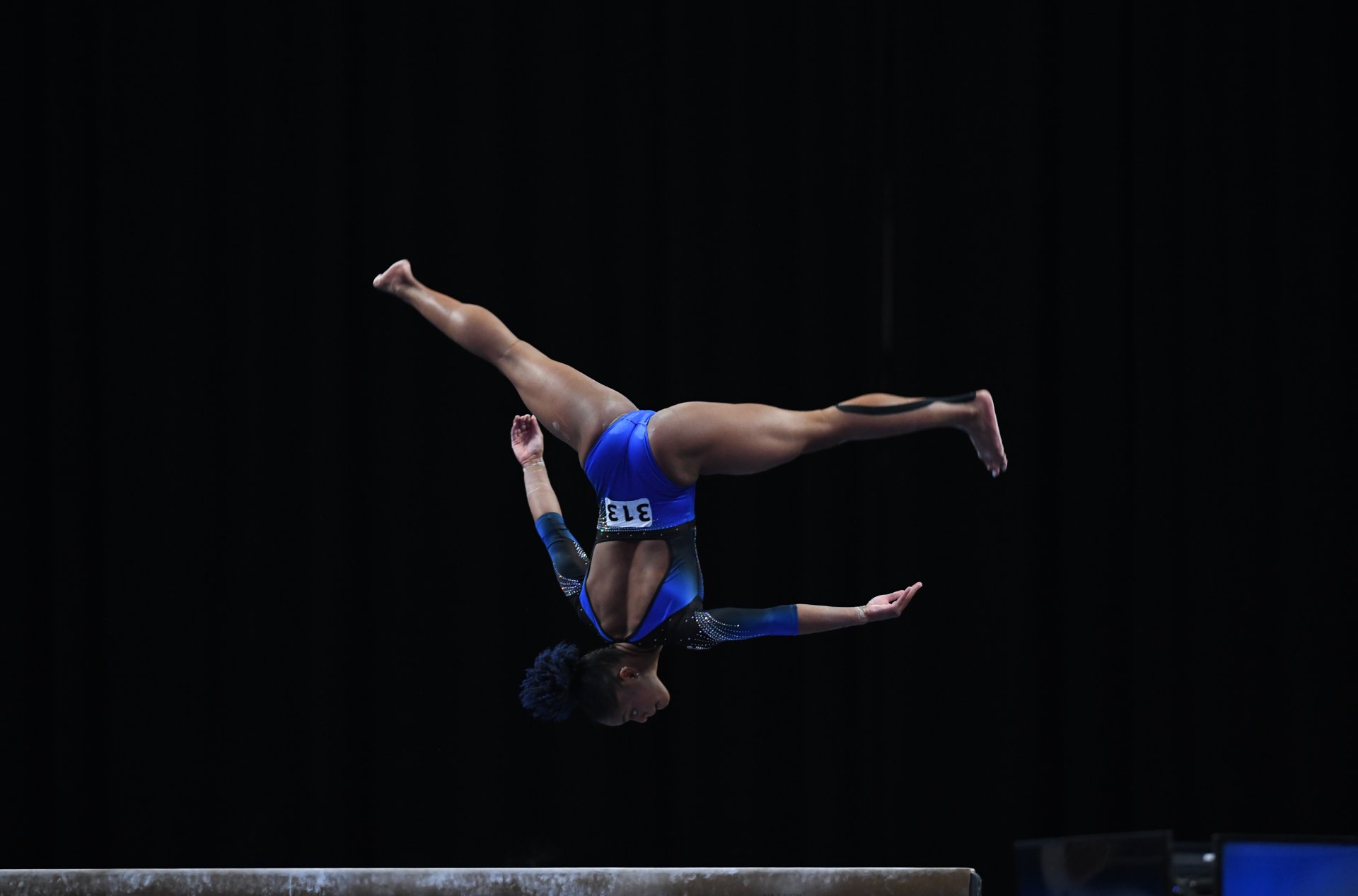 A female gymnast is doing a handstand on a balance beam.
