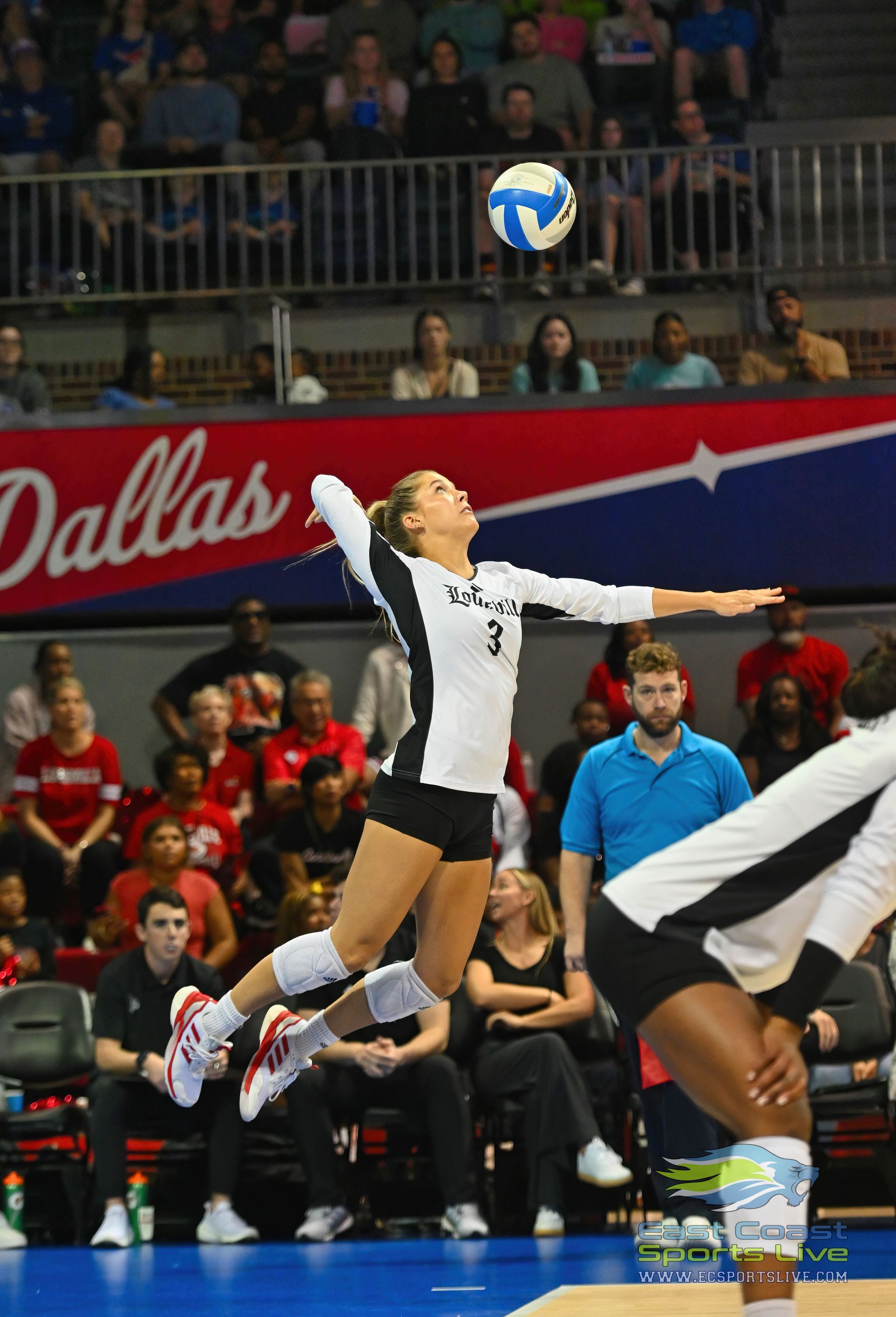 A volleyball game is being played in front of a dallas banner