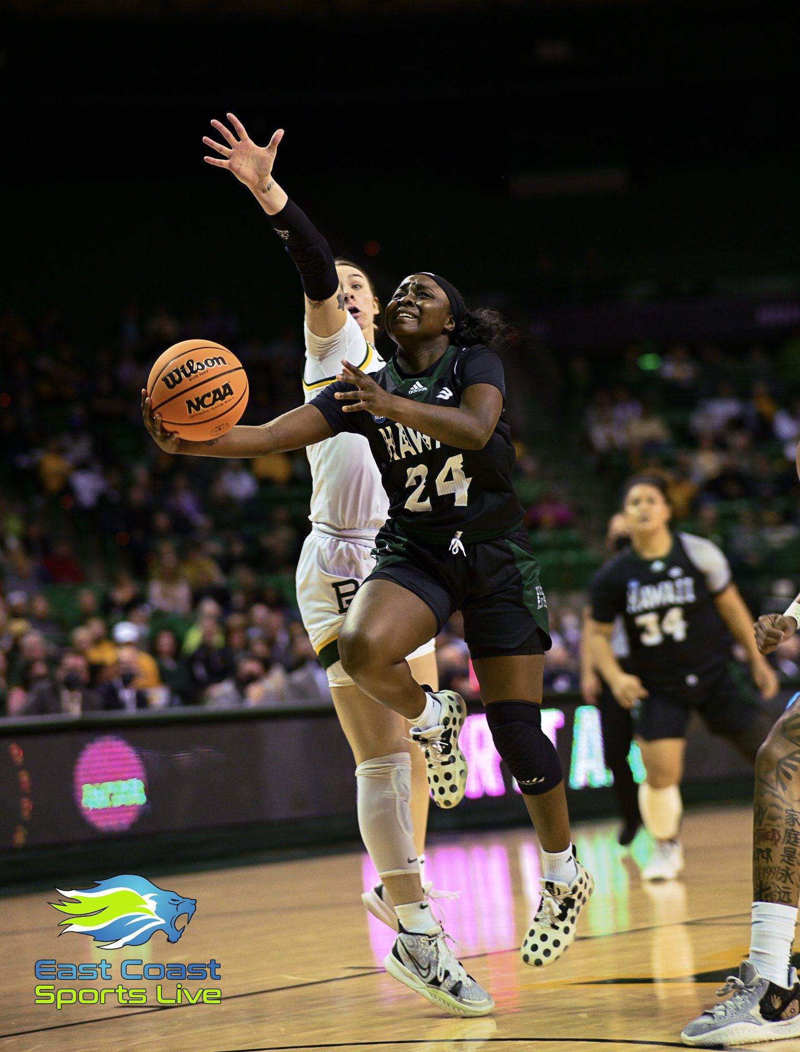 A woman is playing basketball on a court while another woman tries to block her shot.