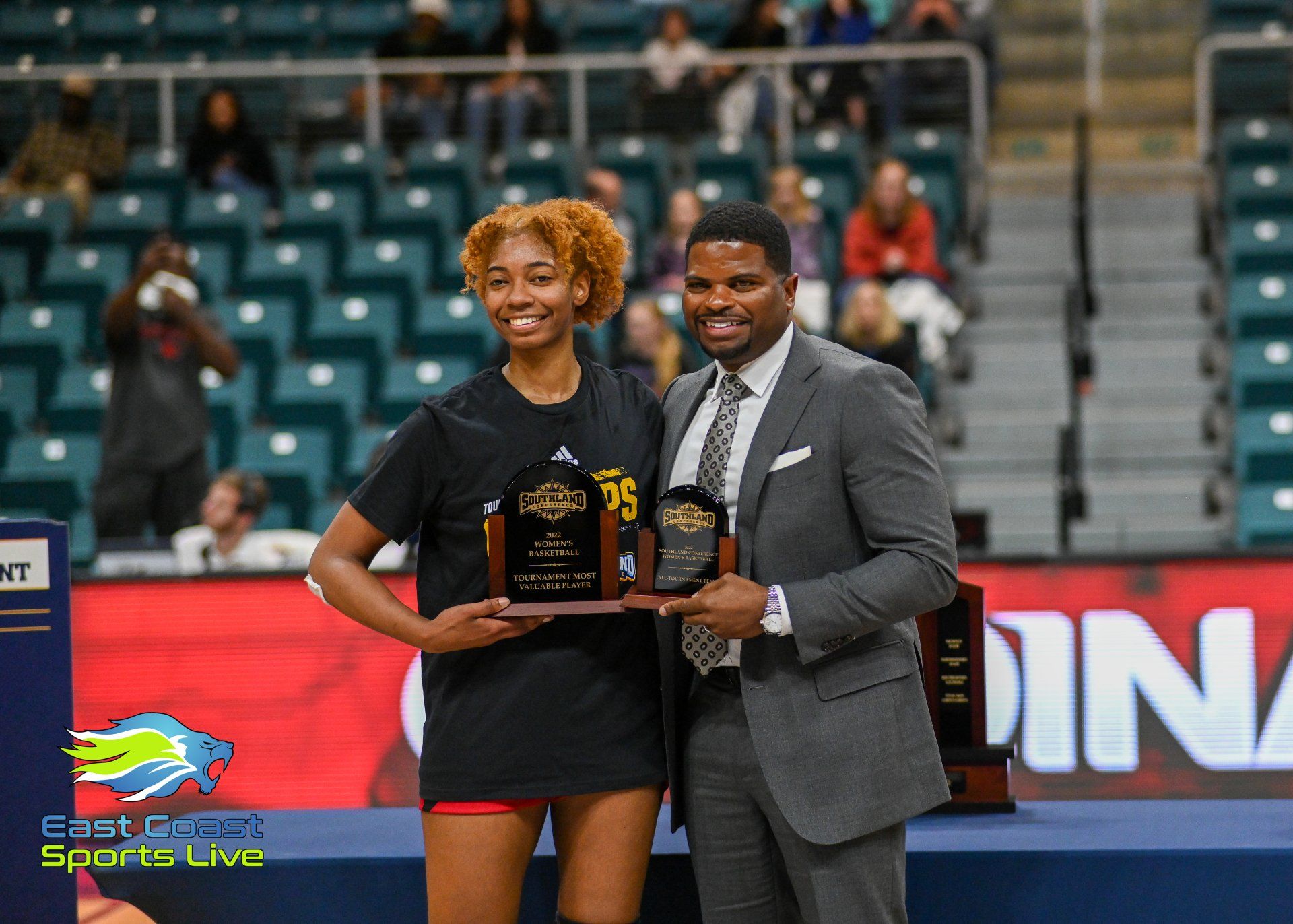 A man in a suit is holding a trophy next to a woman in a black shirt.