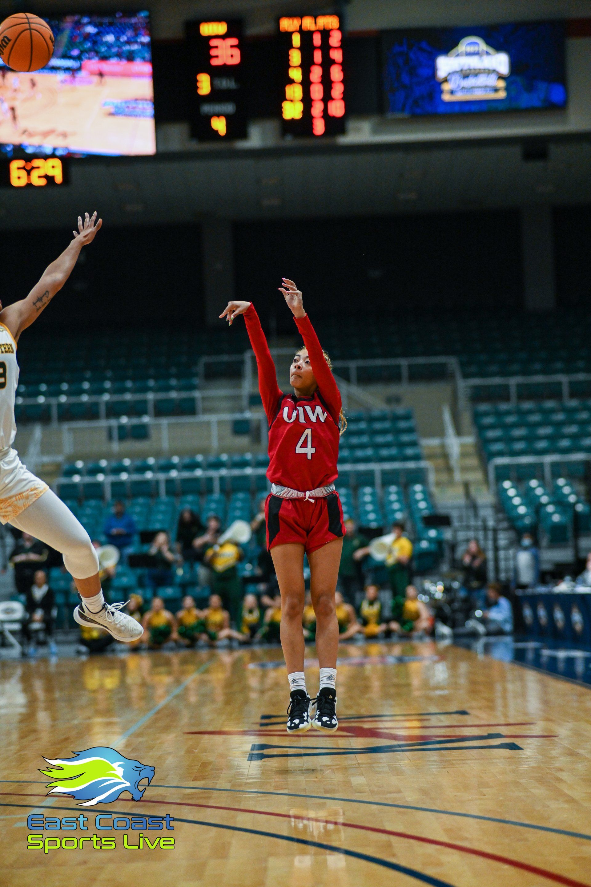 A female basketball player is jumping in the air to throw the ball during a game.