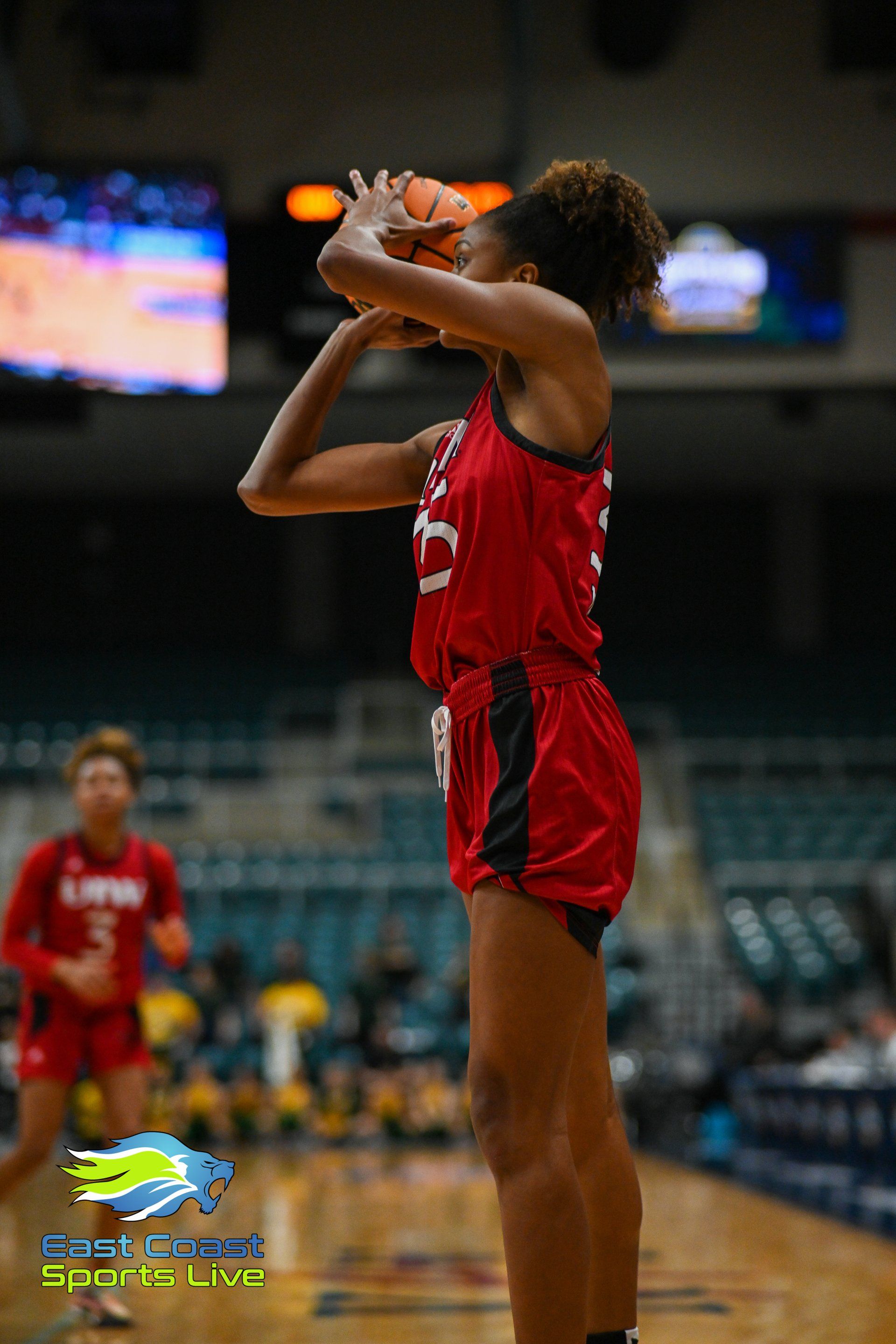 A woman in a red jersey is holding a basketball in her hands on a basketball court.