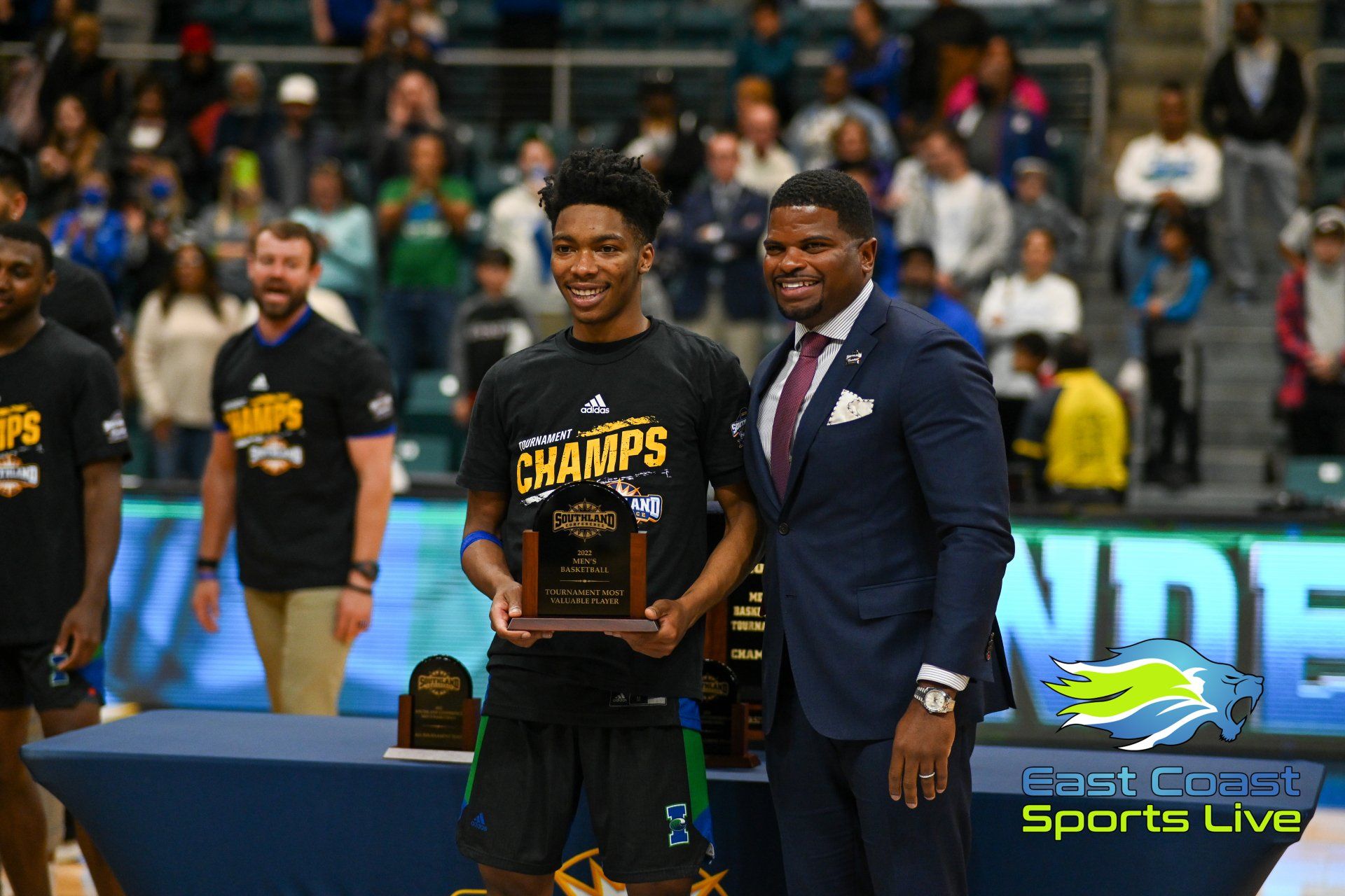 A man in a suit and tie is standing next to a basketball player holding a trophy.