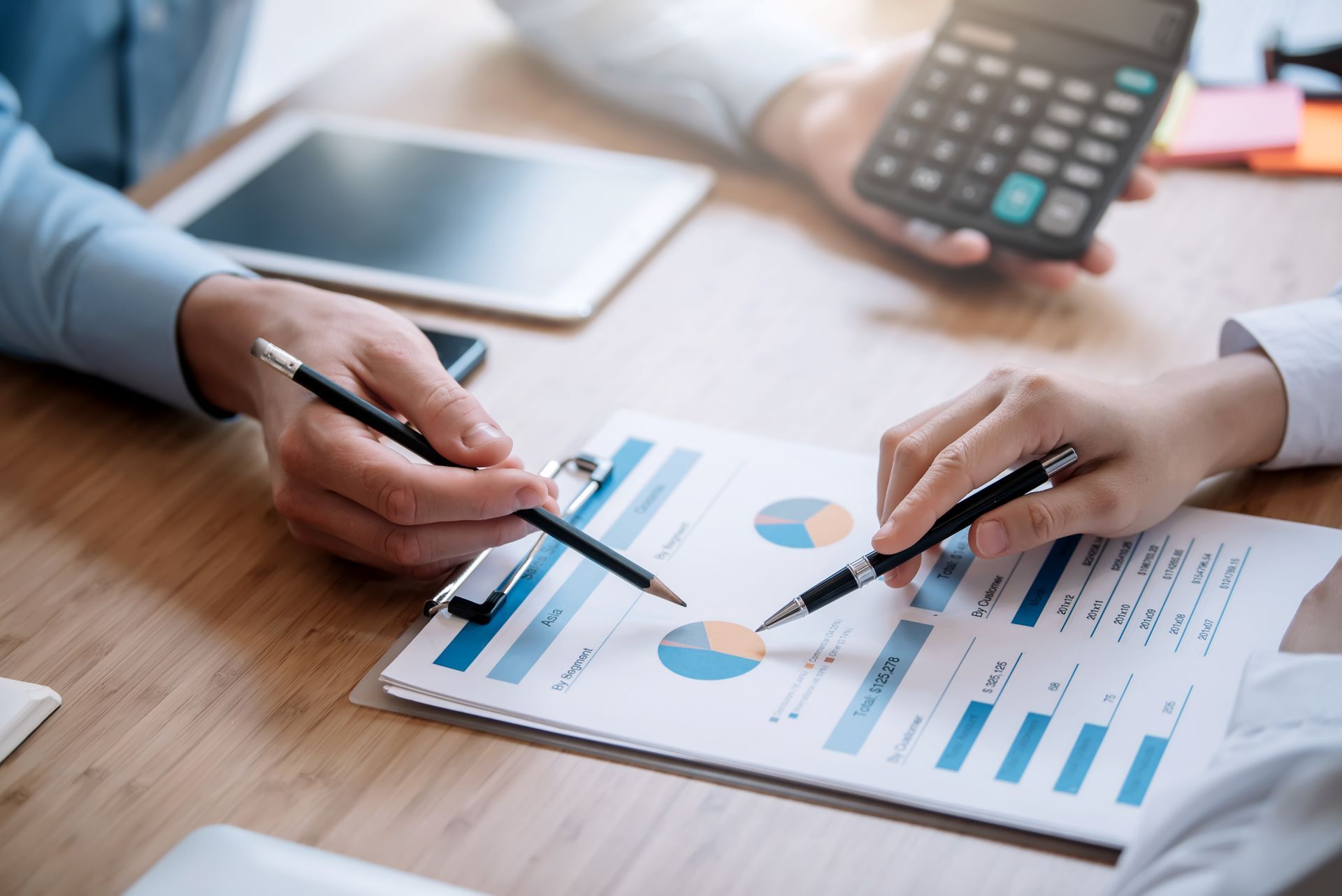 A man is holding a calculator while a woman is pointing at a graph on a piece of paper.