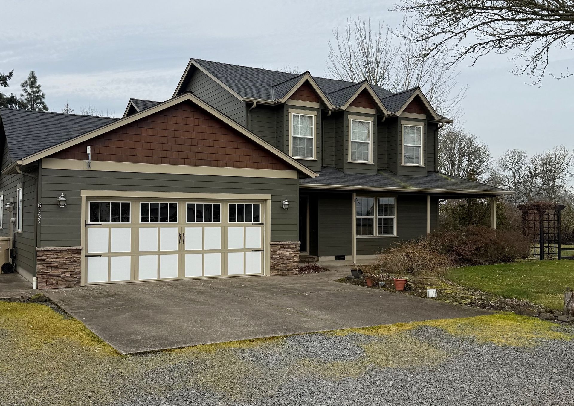 Suburban two-story house with attached garage, gray siding, brown brick, and a gravel driveway