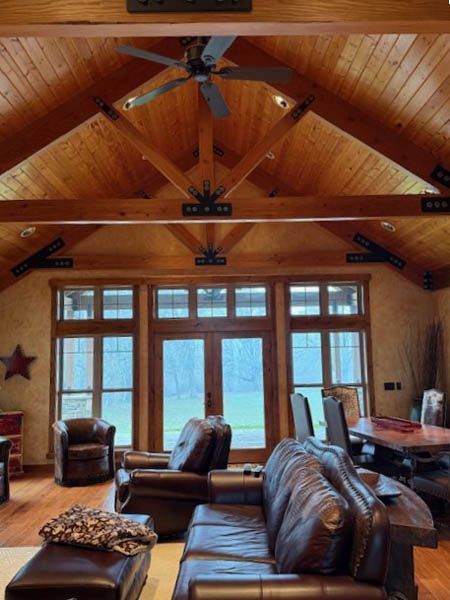 Cozy cabin living room with wood vaulted ceiling, leather seating, and large windows overlooking water