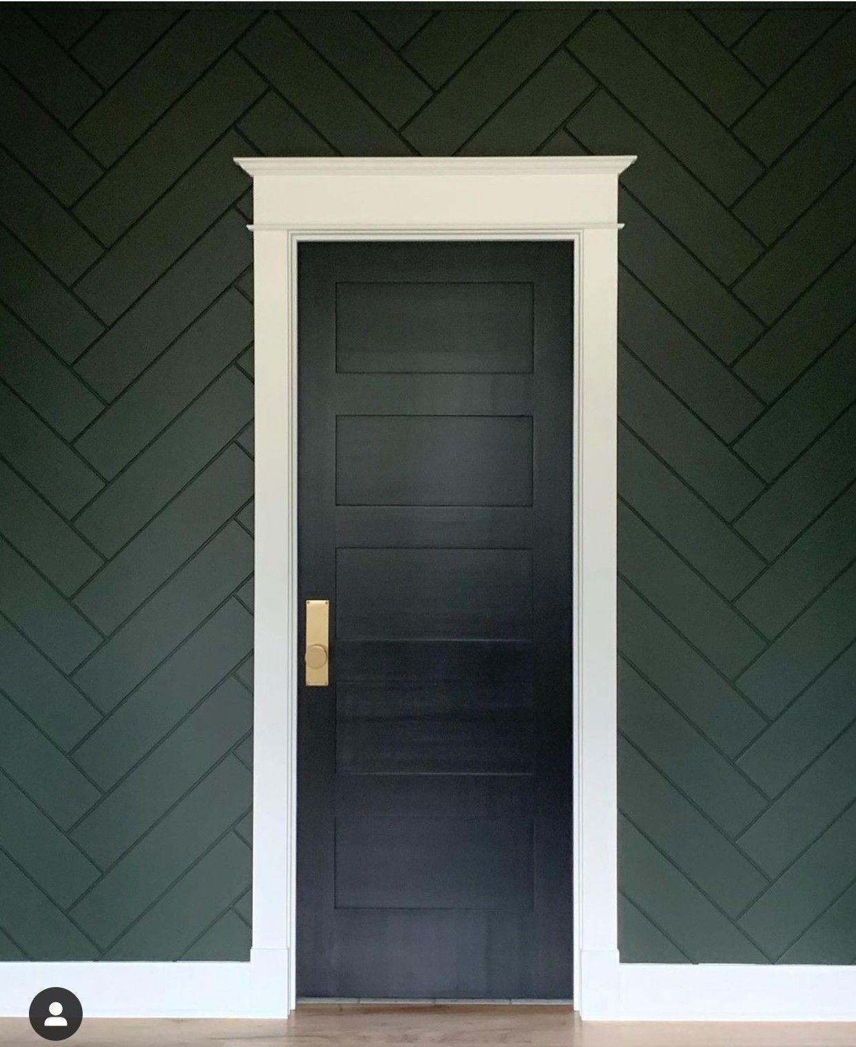 Black door with brass handle framed by white trim against dark green herringbone wall