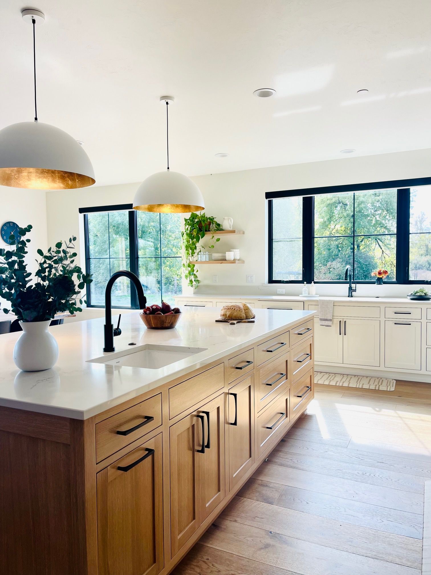 Bright modern kitchen with wood island, white cabinets, pendant lights, and large windows.