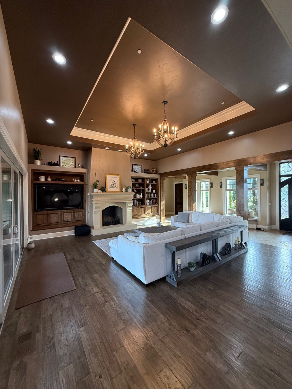 Elegant living room with vaulted ceiling, fireplace, chandelier, sectional sofa, and large windows