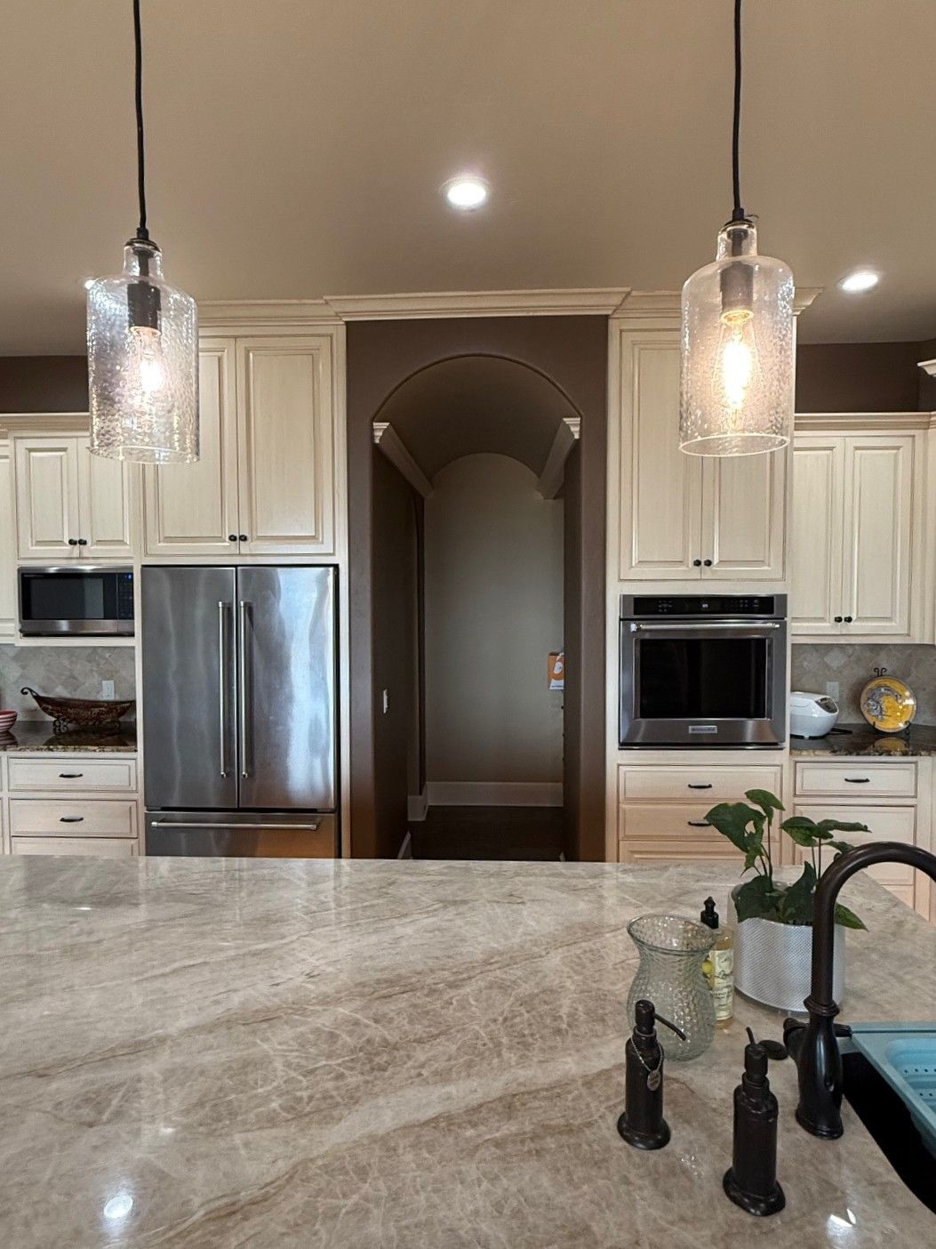Modern kitchen with marble island, pendant lights, stainless appliances, and hallway archway.